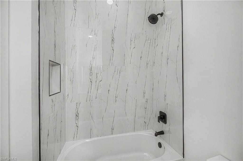 Built-in bathtub with black fixtures, large-format tile surround, and an integrated shower niche