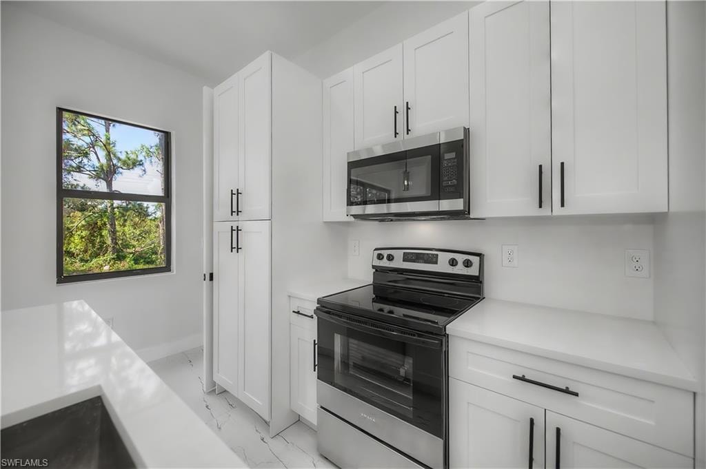 Modern kitchen featuring white shaker cabinetry, stainless steel appliances, white countertops, and wood-finish flooring