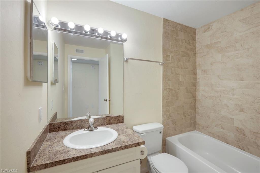 Bathroom with vanity, visible vents, toilet, and shower / washtub combination