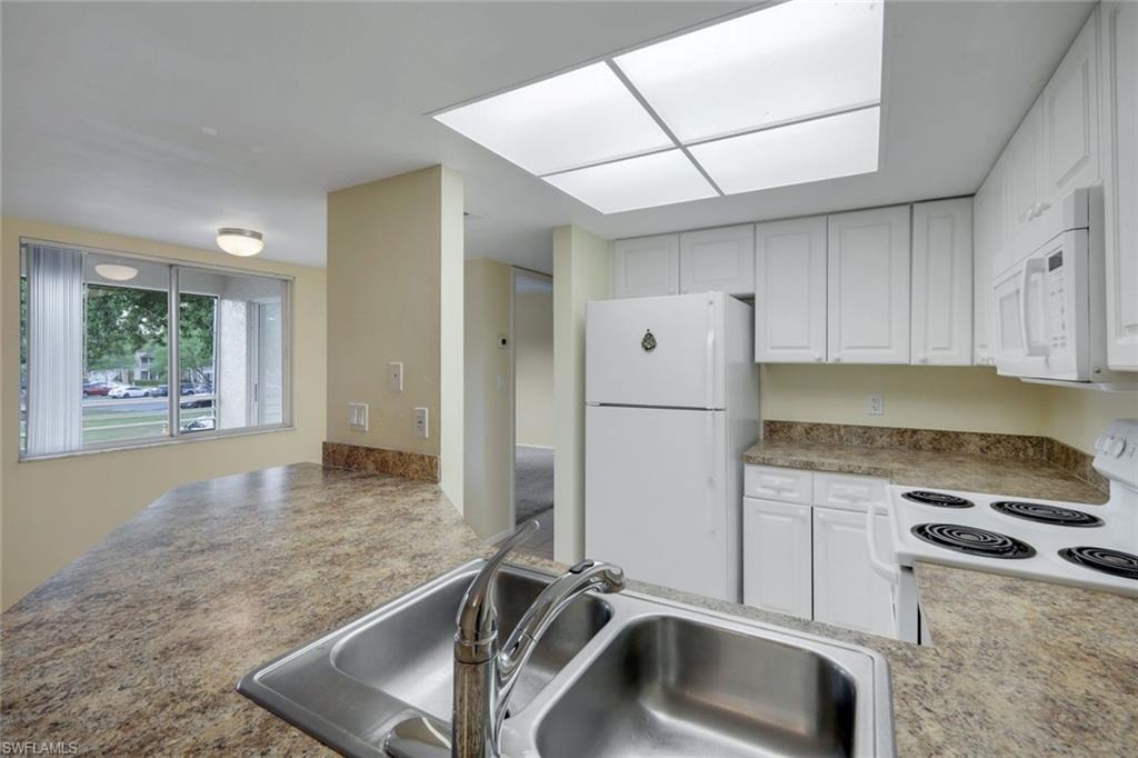 Kitchen with a sink, white cabinetry, and white appliances