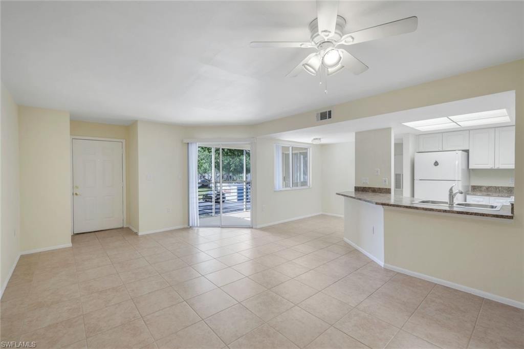 Unfurnished living room featuring baseboards, light tile patterned floors, visible vents, ceiling fan, and a sink