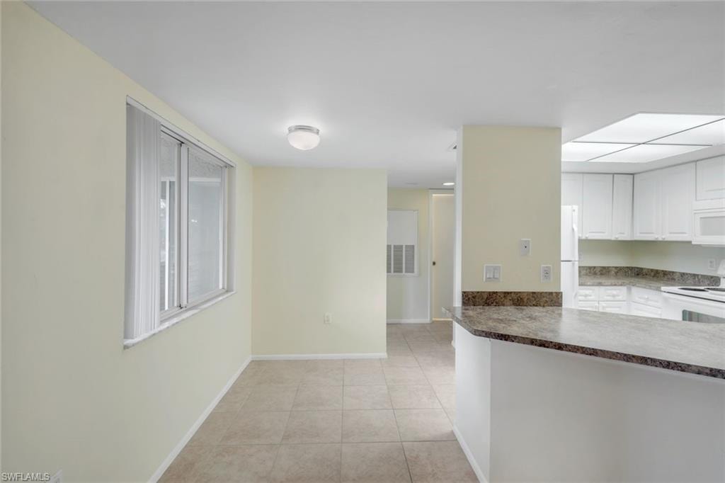 Kitchen with light tile patterned floors, white appliances, white cabinetry, dark countertops, and baseboards