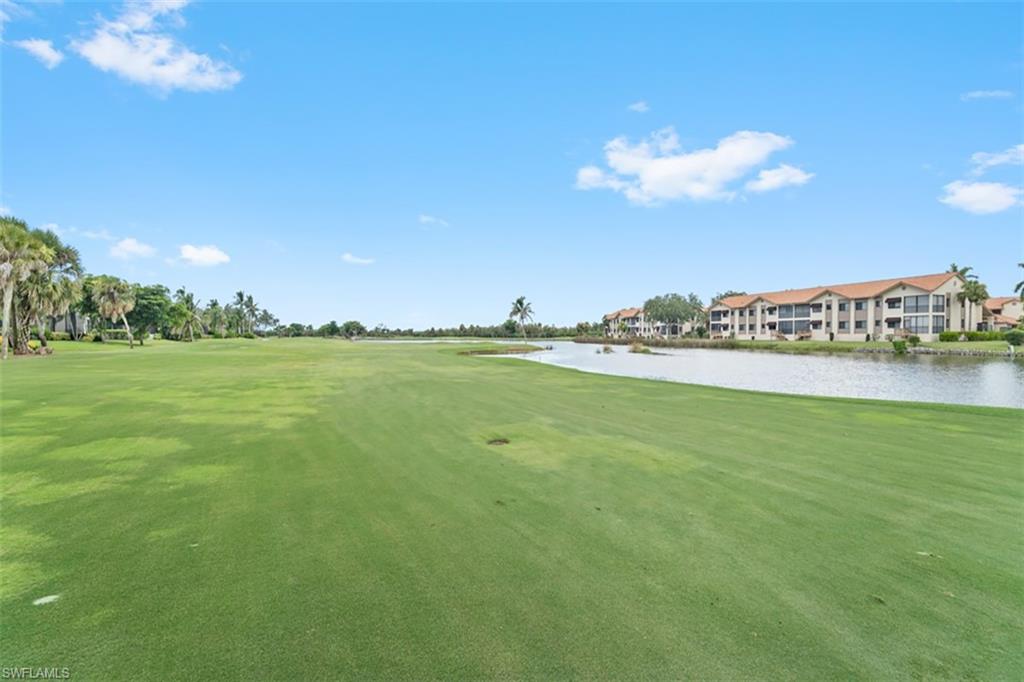 Expansive green space featuring a water element, mature palm trees, and multi-story buildings with terracotta-style roofs