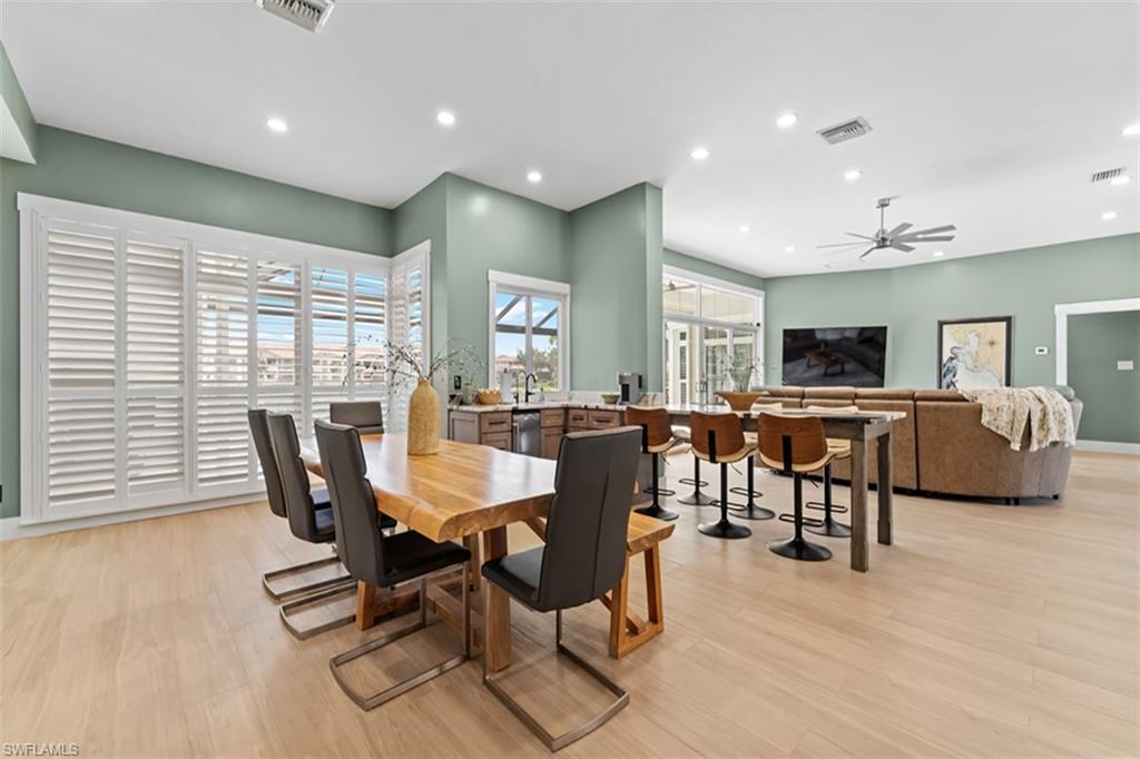 Open-concept living space featuring light wood-finish flooring, recessed lighting, and expansive windows with plantation shutters