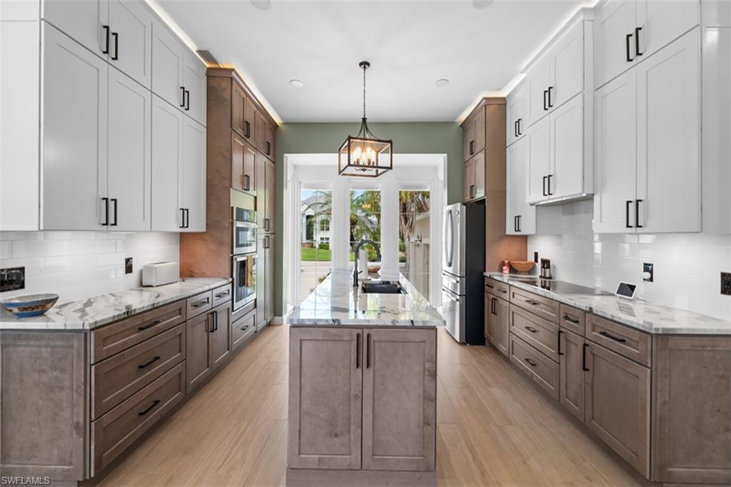 Spacious kitchen featuring an expansive center island, light wood-finish flooring, white upper cabinetry, white subway tile backsplash, and built-in stainless steel appliances