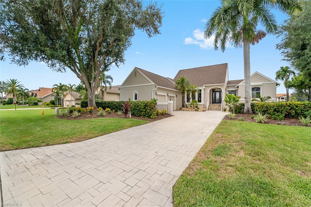Stucco exterior, stamped concrete driveway, mature landscaping, and an arched entry with a dark-framed door