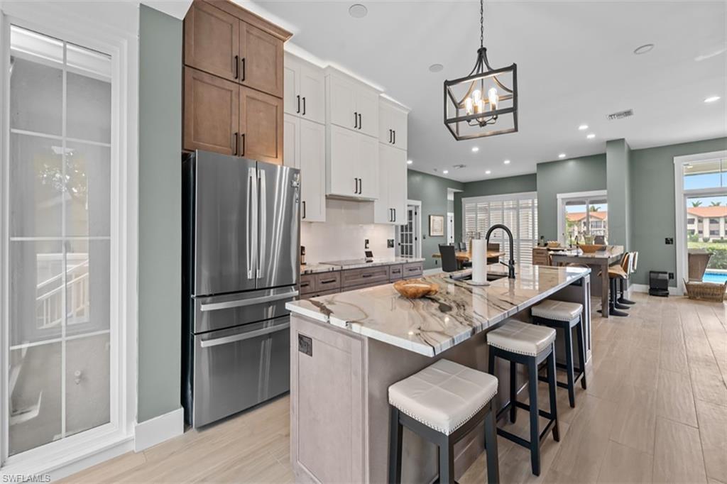Expansive kitchen featuring a large island with a waterfall-edge countertop, stainless steel appliances, two-tone cabinetry, and wood-finish flooring