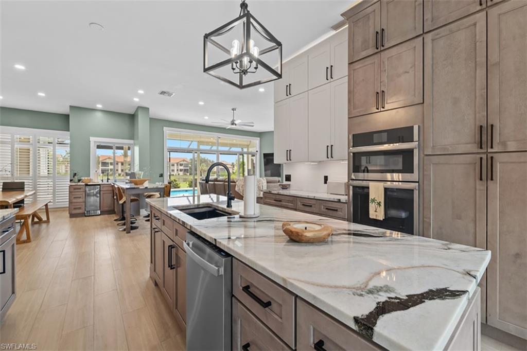 Kitchen featuring a large island with a substantial countertop, built-in stainless steel appliances, pendant lighting, wood-finish flooring, and a screened outdoor area with a pool