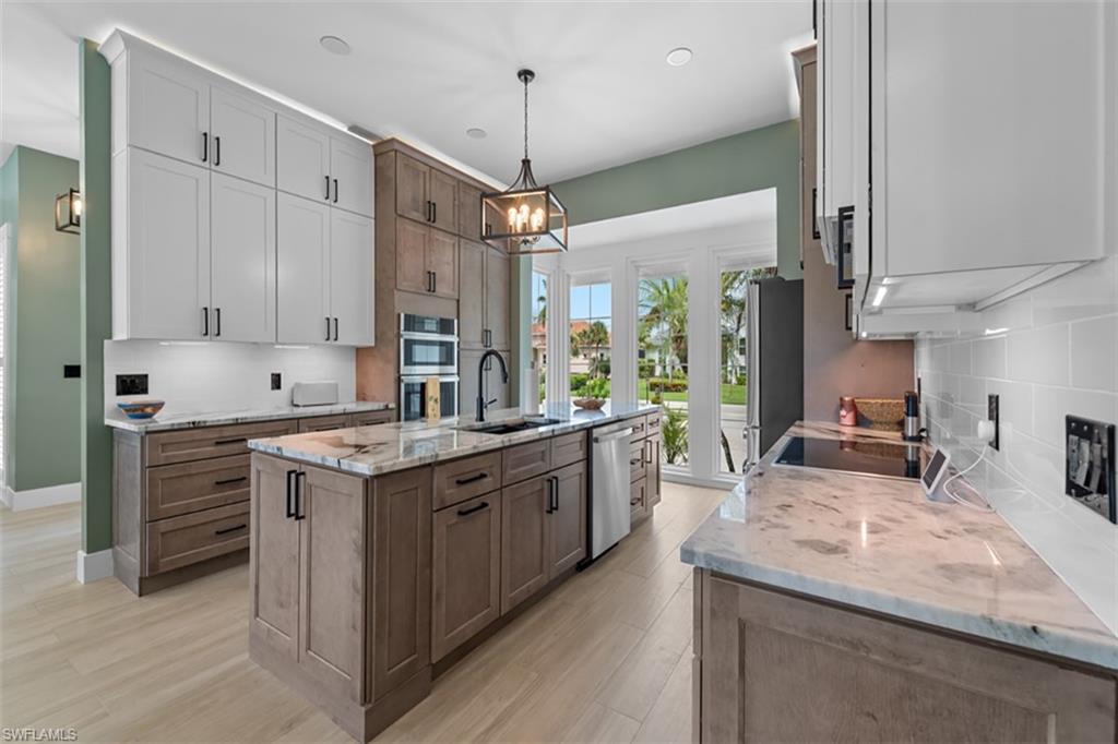 Kitchen featuring a large island with a sink, built-in wall oven, cooktop, and light-toned flooring