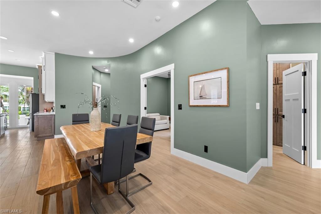 Open-concept dining area with wood-finish flooring, recessed lighting, and a soft green painted accent wall