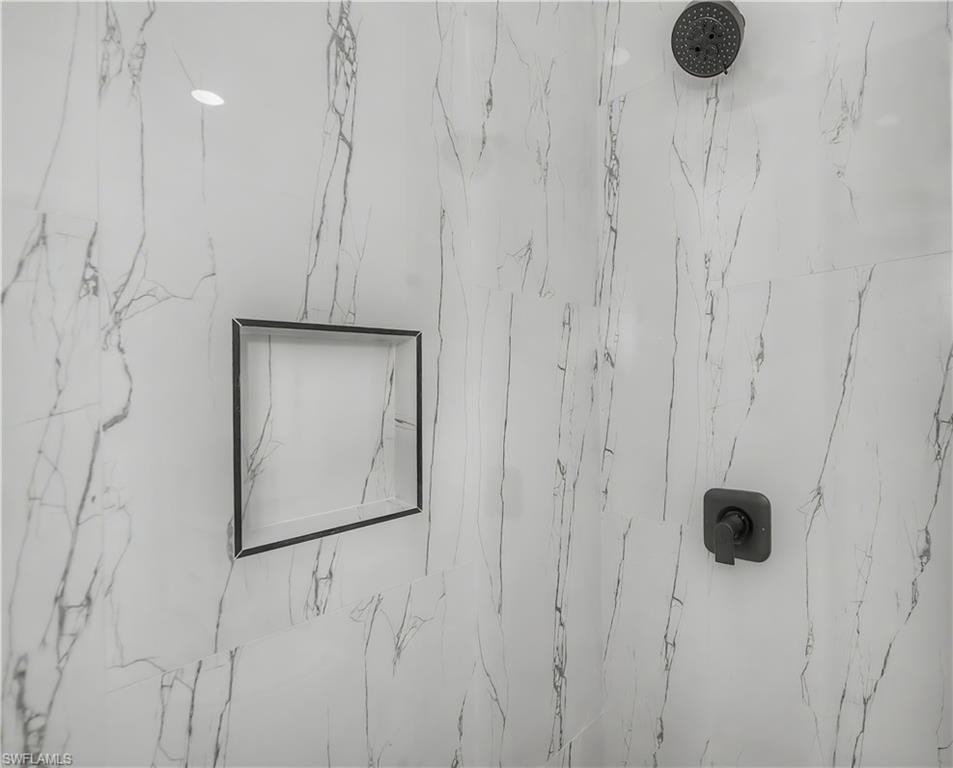 Shower enclosure with marble-look tile, a matte black rain shower head, a built-in shower niche, and a matte black shower control