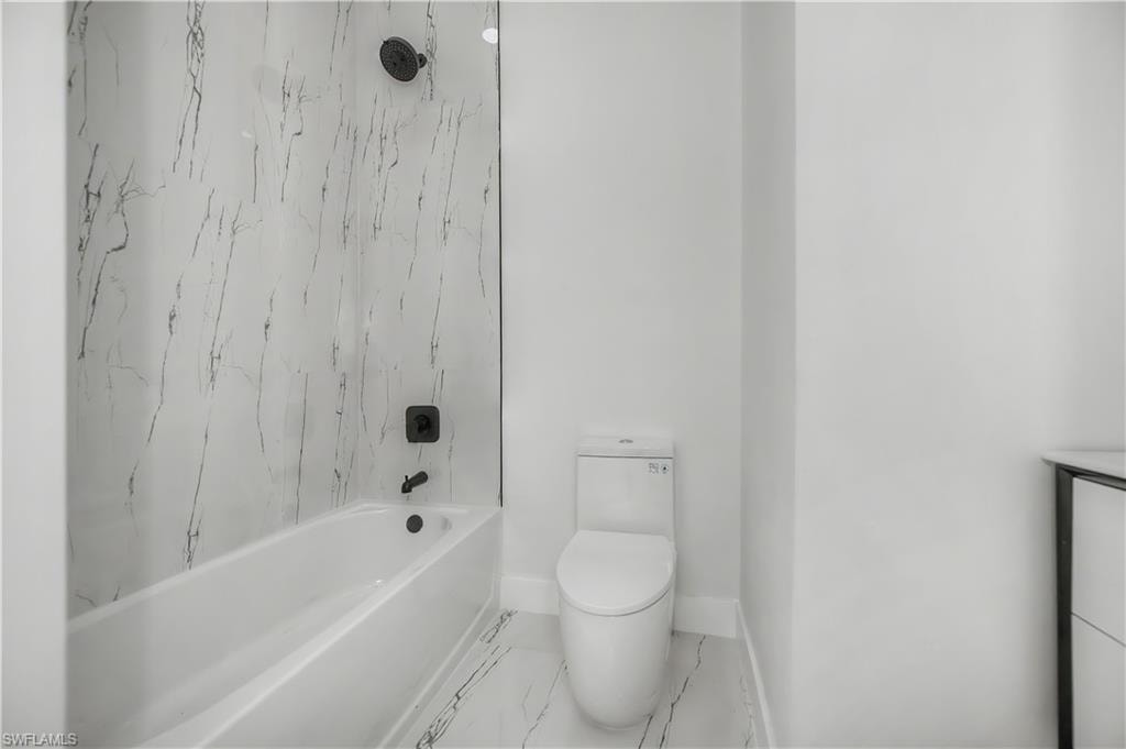 Bathtub with a shower, marble-look wall tiling, and a black-finish shower system