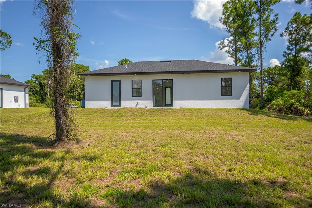 New construction residence featuring a stucco exterior, dark roof, and multiple rear-facing windows and a glass door