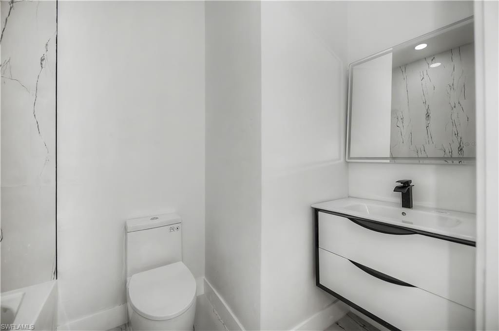 Bathroom featuring a floating vanity with integrated sink, black hardware, wall-mounted mirror, and a white toilet