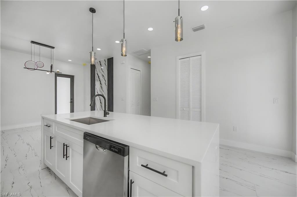 Kitchen island with a white countertop and integrated sink, stainless steel dishwasher, pendant lighting, and white cabinetry with black hardware