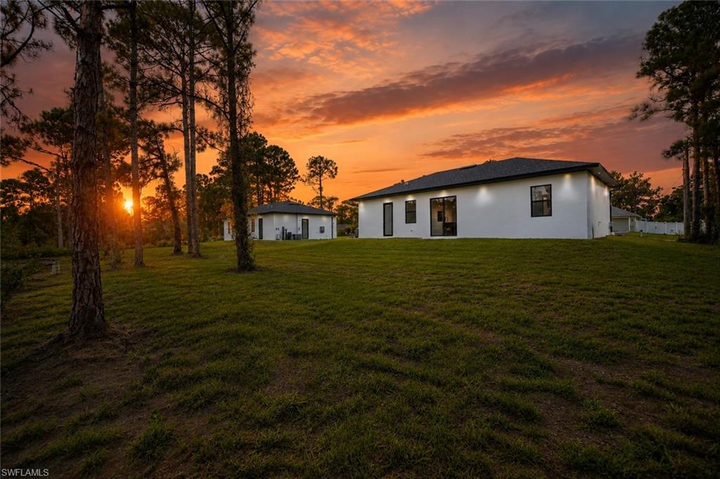 Expansive green lawn with mature trees, a modern white exterior, dark-framed windows, and a dark shingled roof
