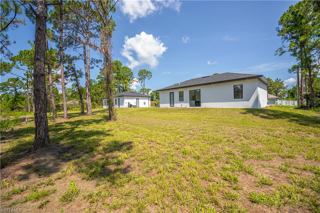 Expansive property featuring a modern white stucco exterior, dark shingle roof, numerous windows with dark frames, and mature pine trees