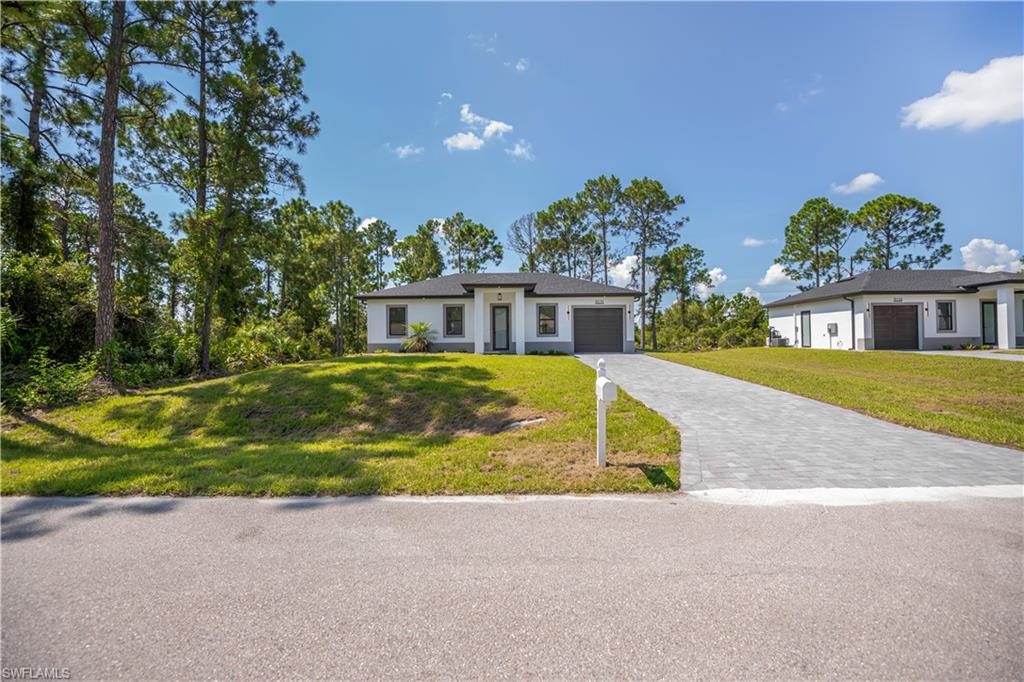 White stucco exterior with dark trim accents, featuring an attached garage and a paved driveway