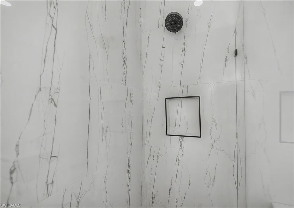 Shower with marble-look tile, dark-finish shower head, and recessed wall niche with dark trim