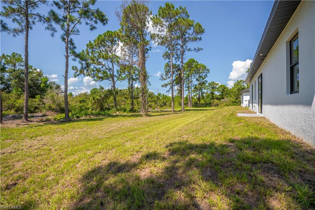 Expansive lawn with mature trees and a white stucco exterior with dark-framed windows