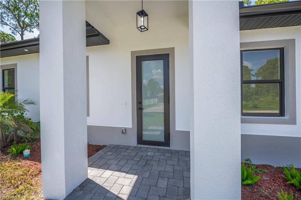 Modern covered entryway featuring white composite columns, dark-framed glass entry door with sidelights, and geometric paver flooring in charcoal tones
