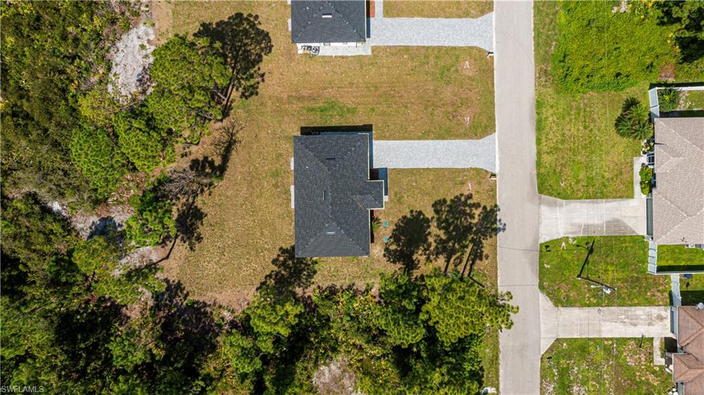 Aerial perspective highlighting a residential property with a dark shingle roof, a light-toned driveway, and surrounding green landscaping