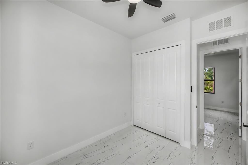 White bi-fold closet doors, ceiling fan, white walls, and marble-look flooring