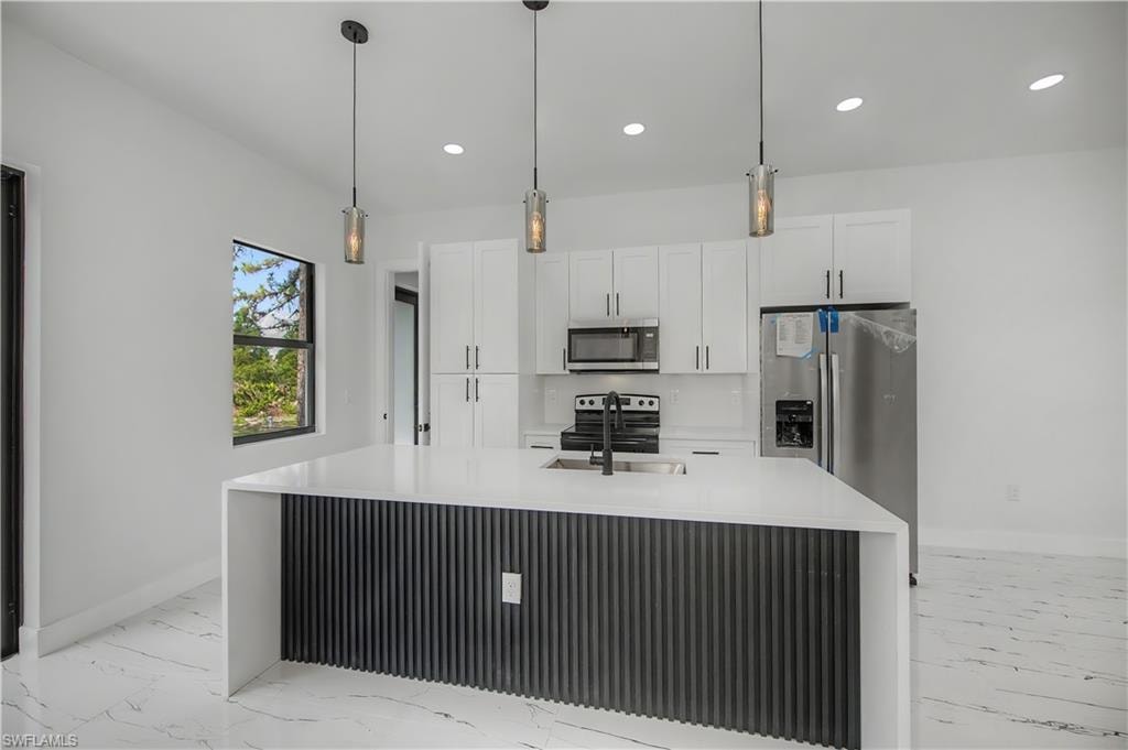 Kitchen featuring white cabinetry, stainless steel appliances, a center island with a sink, pendant lighting, and white tile flooring