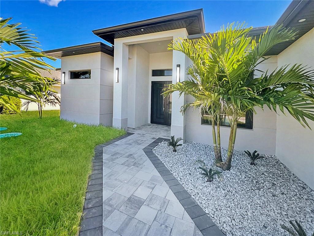 Contemporary exterior featuring a paver walkway, mature palm trees, and well-maintained landscaping with decorative white stone