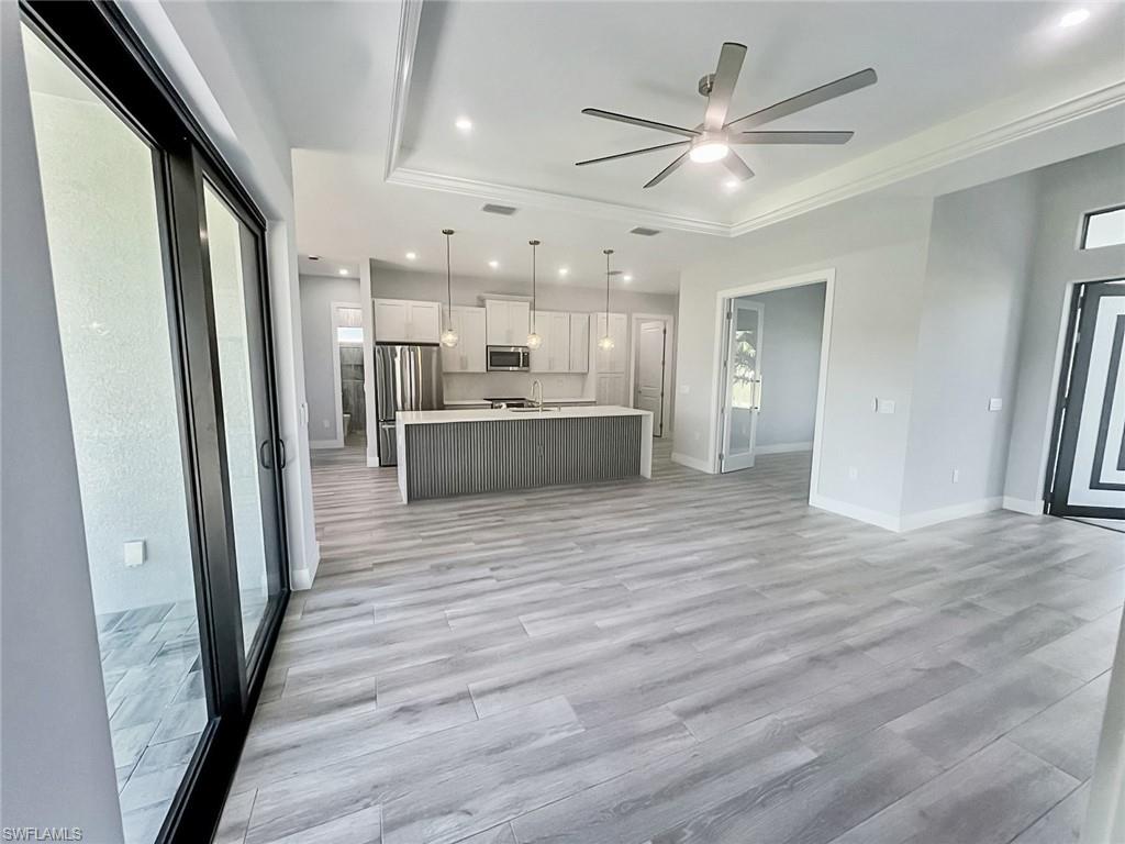 Tray ceiling with recessed lighting and a ceiling fan, light wood-finish flooring, sliding glass doors, white shaker cabinets, and stainless steel appliances
