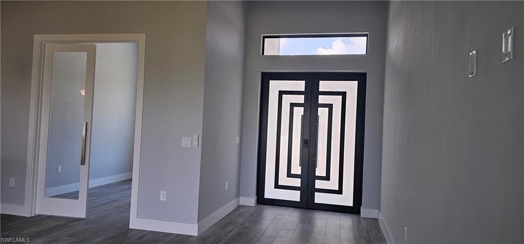 Modern entryway featuring a striking geometric-patterned double-door entrance with transom window, polished concrete flooring, and clean white wall finishes throughout the foyer space