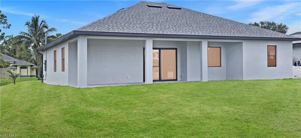 Expansive green lawn, dark shingle roof, light stucco exterior, covered patio, and large sliding glass doors