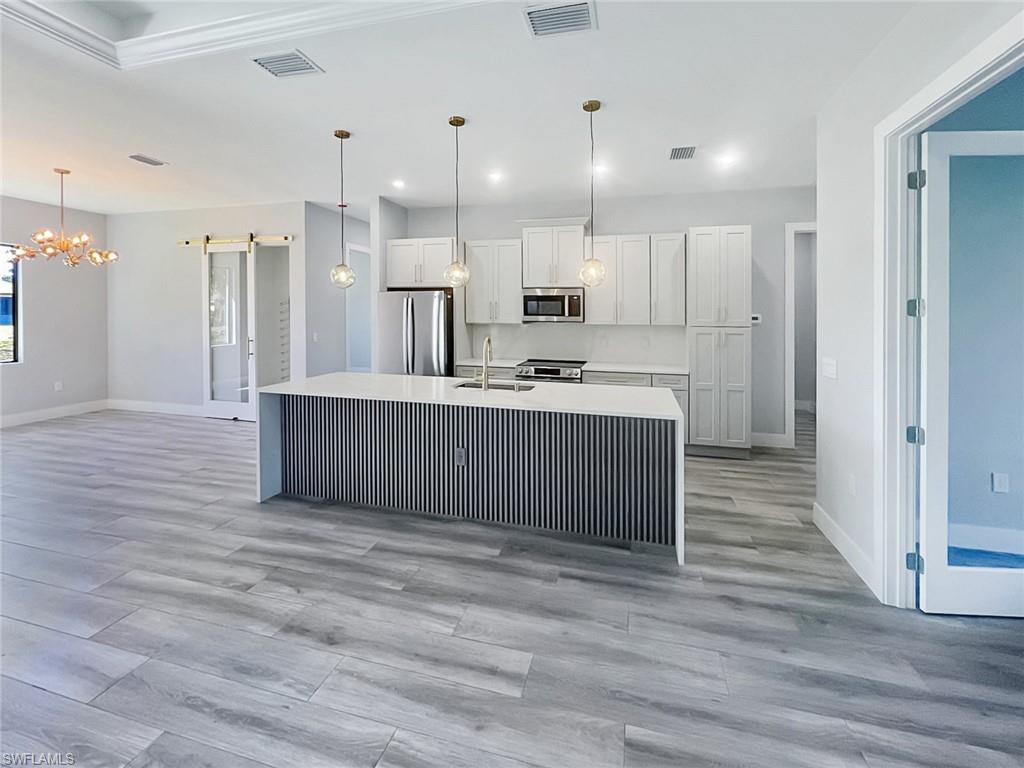 Open-concept kitchen and living area featuring wood-finish flooring, white cabinetry, a kitchen island with a waterfall countertop, stainless steel appliances, and decorative pendant lighting
