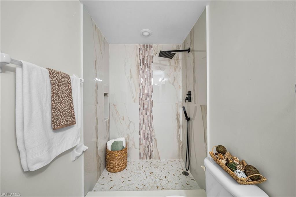 Walk-in shower with full height tile surround, accent tile inlay, a built-in shower niche, and a black finish rain shower head
