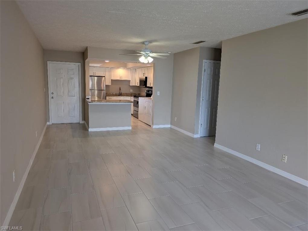 Unfurnished living room with ceiling fan and a textured ceiling