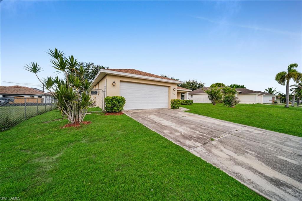 Single-story stucco exterior with an attached garage, featuring a concrete driveway, established landscaping, and a chain-link fence
