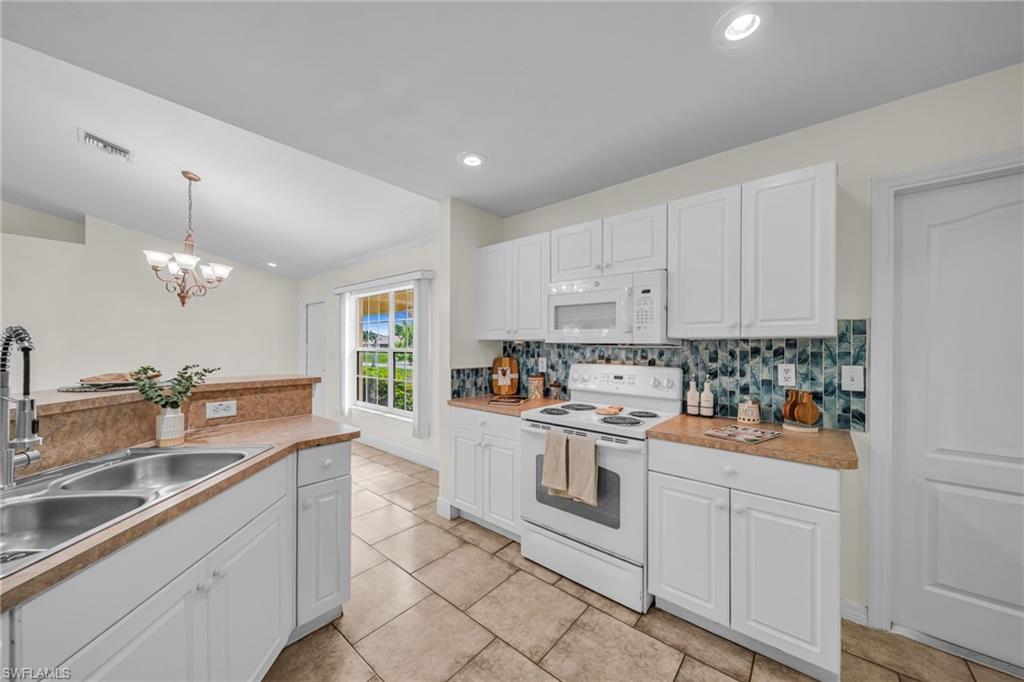 Kitchen featuring white cabinetry, a double basin stainless steel sink, a tile backsplash, and recessed lighting