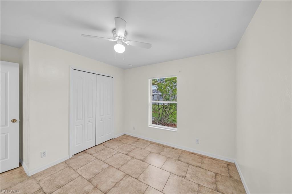 Spacious bedroom featuring tile flooring, a ceiling fan with integrated lighting, large window with natural light, and dual closet doors for ample storage