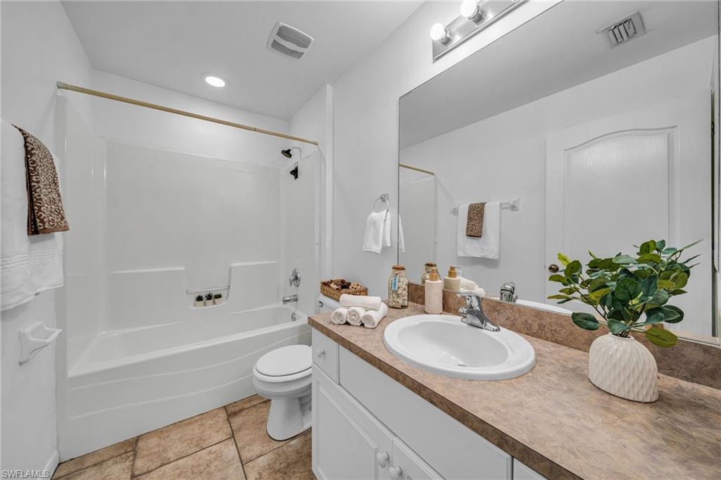 White bathtub and shower combination, single vanity with integrated sink, expansive vanity mirror, and tile flooring