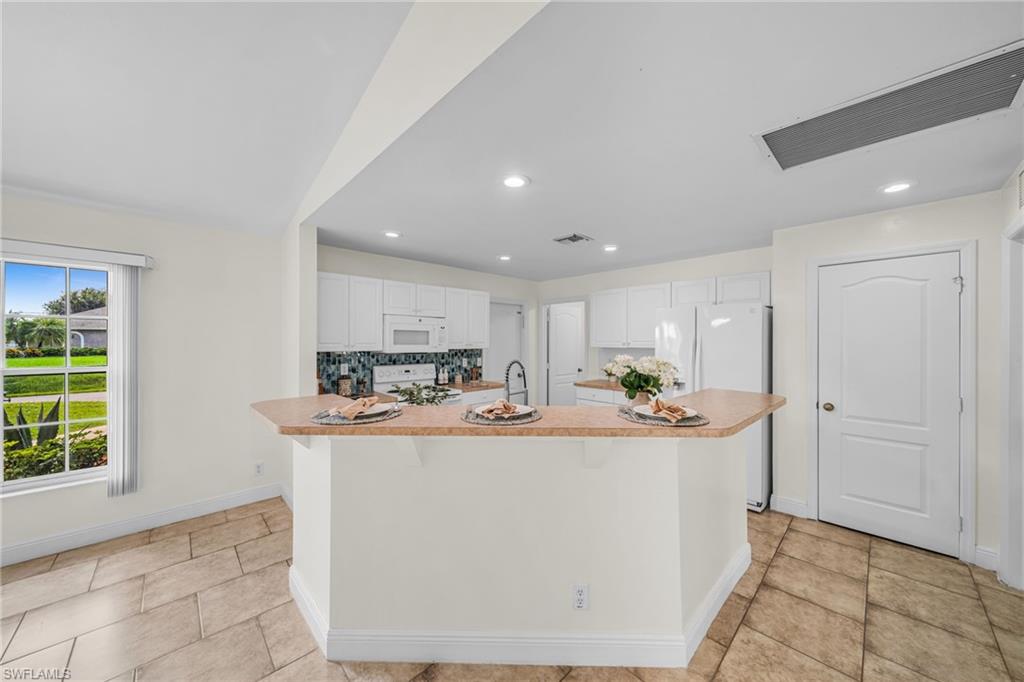 Kitchen featuring white cabinetry, white appliances, a tiled backsplash, and a breakfast bar