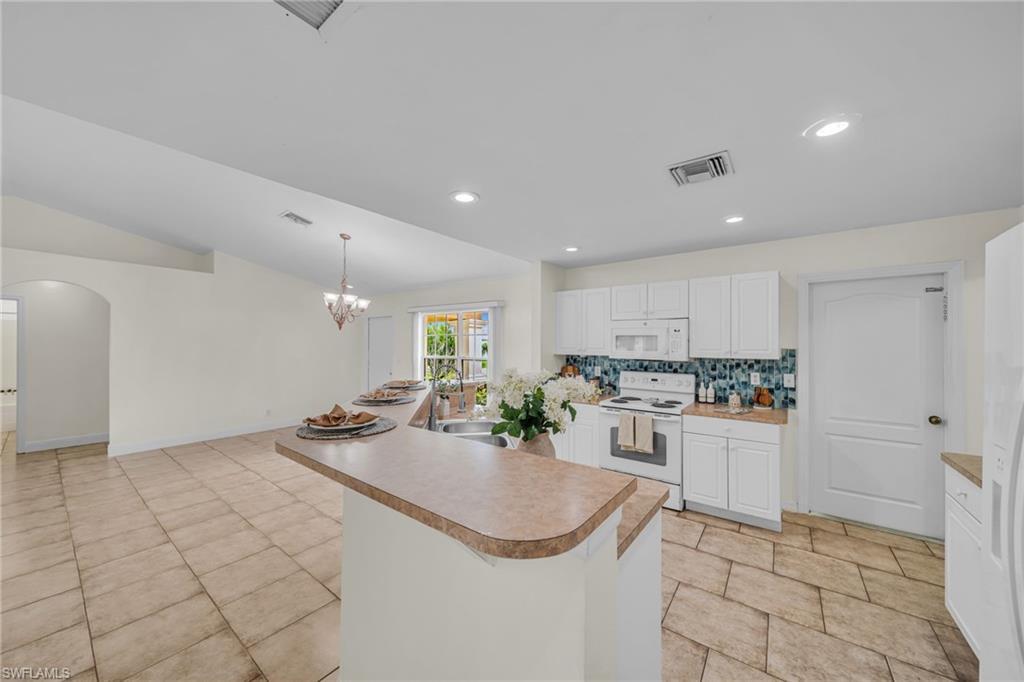 Kitchen island with integrated sink, white cabinetry, a tiled backsplash, recessed lighting, and tile flooring