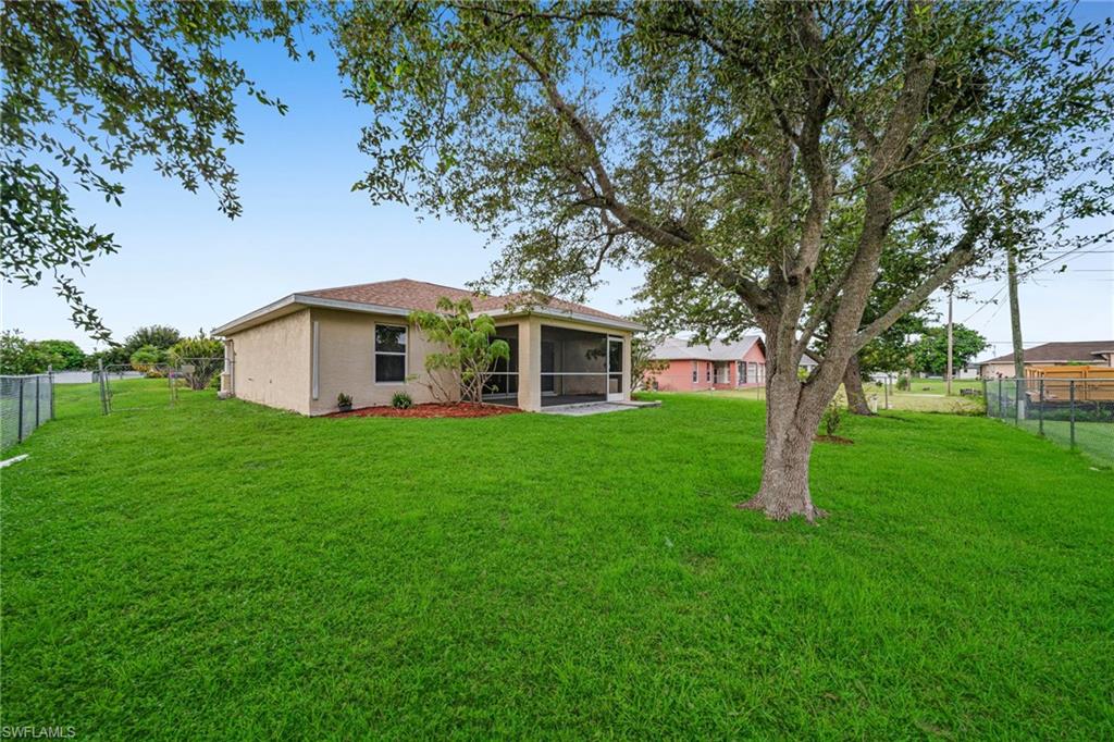 Expansive green lawn, mature tree, chain-link perimeter fencing, rear screened-in patio, and stucco exterior