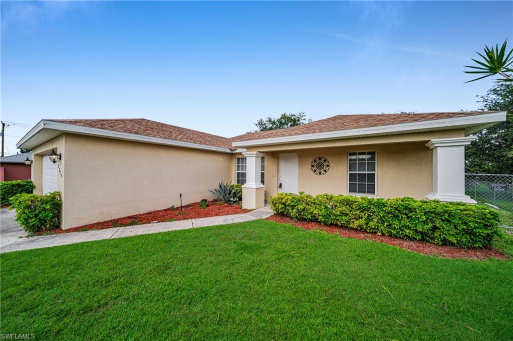 Stucco exterior with a shingle roof, attached garage, concrete walkway, and decorative landscaping
