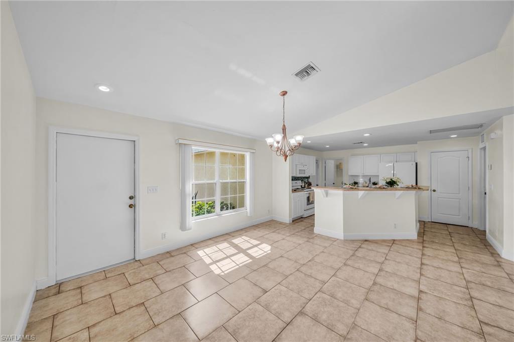 Vaulted ceiling with recessed lighting, large window with blinds, tiled flooring, kitchen island with counter seating, and white kitchen cabinetry