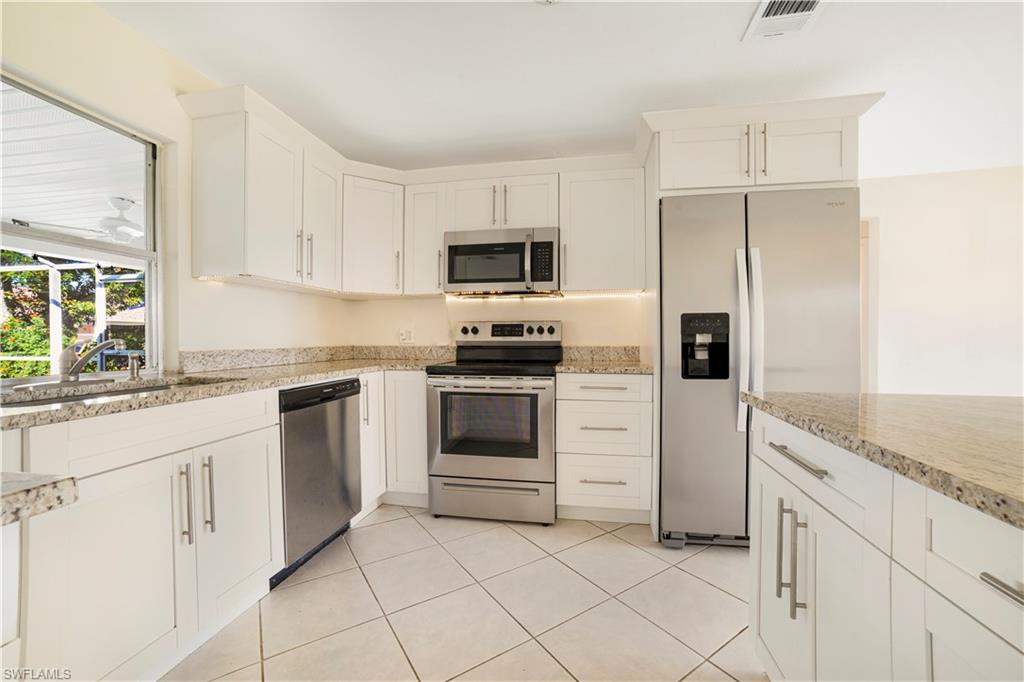 Kitchen with stainless steel appliances, light stone countertops, white cabinets, and sink