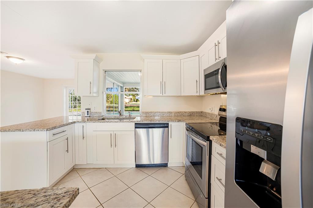 Kitchen with white cabinets, light tile patterned flooring, light stone counters, and appliances with stainless steel finishes