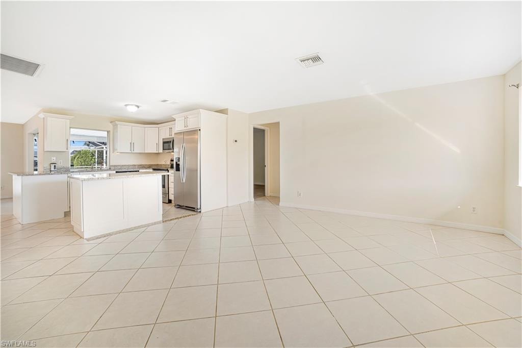 Kitchen featuring white cabinets, appliances with stainless steel finishes, light tile patterned floors, and a center island