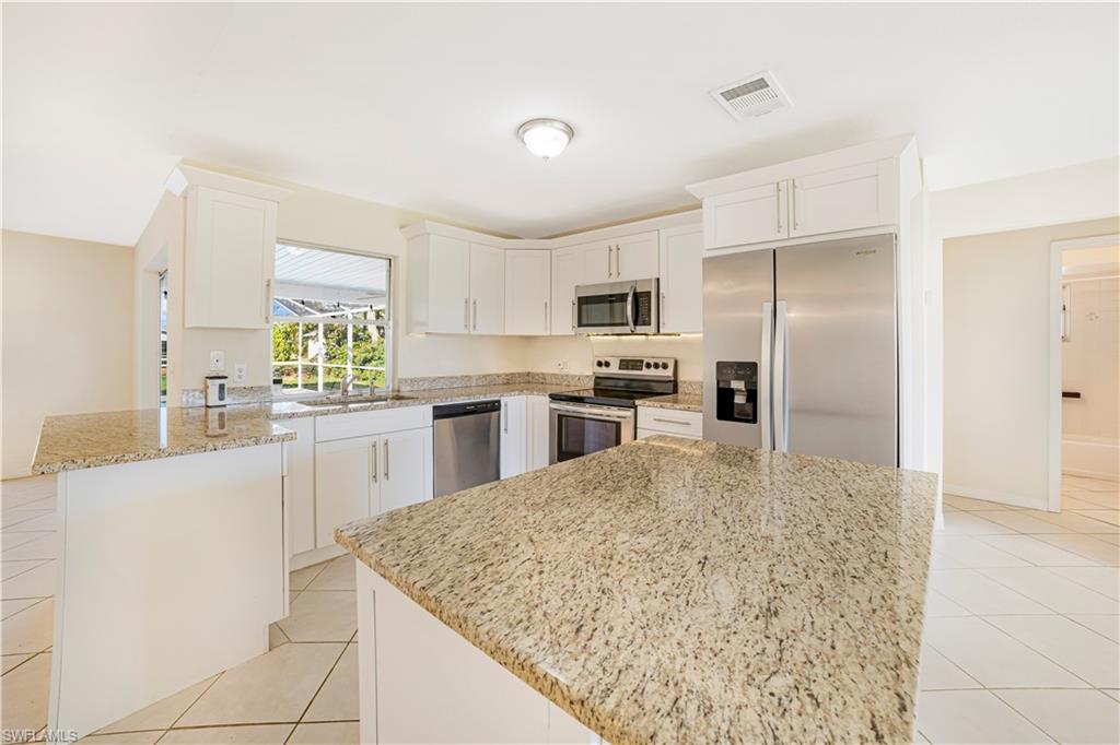 Kitchen featuring white cabinets, a kitchen island, light stone counters, and appliances with stainless steel finishes