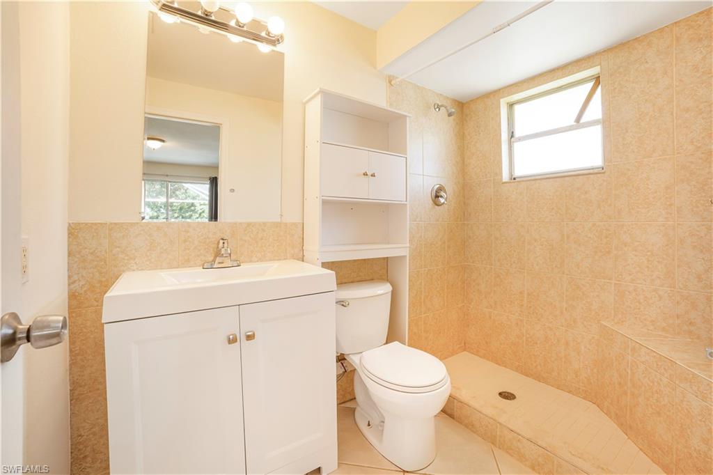 Bathroom with vanity, tiled shower, tile patterned floors, toilet, and tile walls
