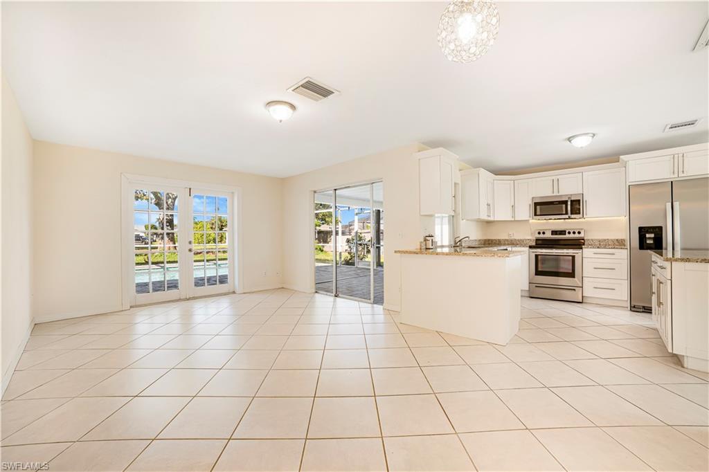 Kitchen with light stone countertops, appliances with stainless steel finishes, light tile patterned flooring, and white cabinets